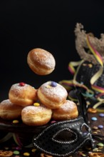 Berliners, doughnuts with icing sugar and Smarties next to a black mask, carnival