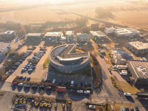 Round building in an industrial area with parked cars and street in the background in sunny