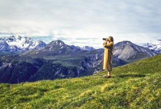 Woman standing on hillside using binoculars in mountains of national park, Western Rhaetian Alps,