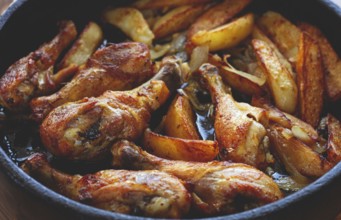 Fried chicken drumsticks with potato slices, in a clay pan, baked in the oven, with spices,