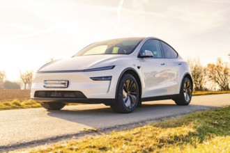 White electric car on a country road in sunny weather and open field, Tesla, New Model Y Juniper,
