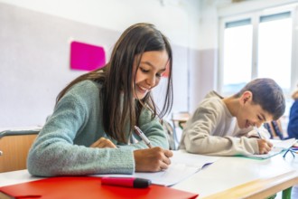 Happy elementary age children writing enthusiastically in notebooks during class, engaging with