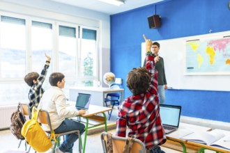 Group of elementary school students raising hands to answer teacher's question in geography class