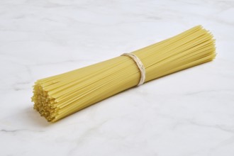 A tightly bound bundle of uncooked spaghetti on a smooth light marble surface