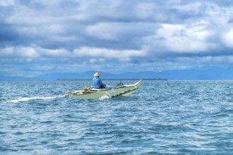 Traditional outrigger boat sailing on turquoise water with a fisherman wearing a straw hat, near