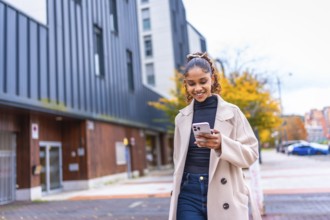 Happy stylish african american young woman using phone walking in the city in autumn