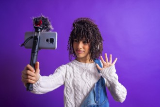 Young influencer waving while recording a video blog using a smartphone with external microphone on