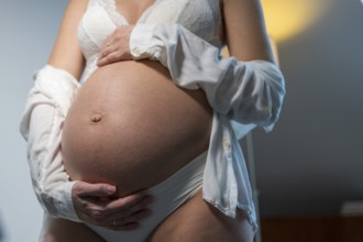 Close-up of a pregnant woman in white underwear holding her belly