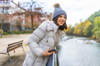 Side view of a beauty woman in winter clothes enjoying river views from the rail in the city