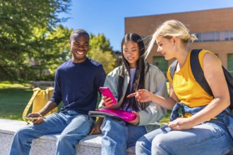 Three male and female multi-ethnic students sitting using mobile in the campus