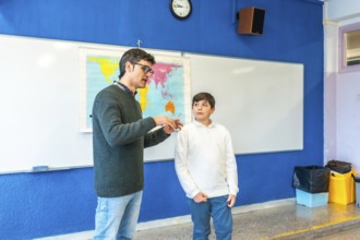 Geography teacher explaining lesson to elementary school student using a world map in a classroom