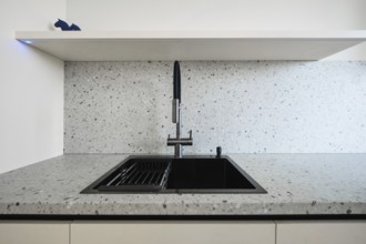A sleek kitchen showcases a contemporary sink with a black finish, set against a light speckled