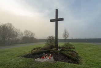 Simple wooden cross in foggy cemetery with red and white votive candles at its base