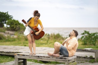 Man touches his chest in emotion as he listens to his girlfriend play guitar