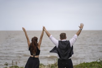 View of a couple from behind celebrating with their arms raised looking at the horizon in the sea