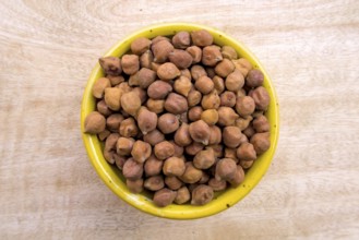 Flat Lay of Black Brown Chickpeas in a Yellow Bowl on Neutral Wooden Background, Top View