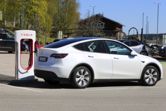 White Tesla Model Y AWD electric car charging battery at Tesla Supercharger station in Salo,
