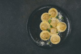 Fresh ravioli with cheese and microgreens, on a black plate, top view, no people