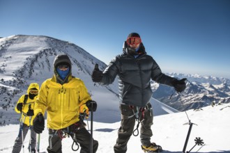 A middle-aged climber in a down jacket and harness shows a thumb up next to his friends on the way
