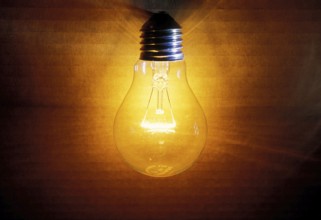 Closeup of an old burning light bulb, switched on, a carton as background is illuminated, lit with