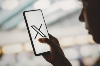 In this photo illustration, a silhouetted woman holds a smartphone with the Twitter (X) new logo