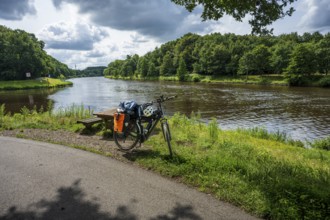 A bicycle stands on a cycle path next to a peaceful river in nature, cycle tour along the Ems and