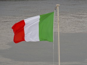Italian flag waving in the wind in front of a body of water, naples, mediterranean sea, italy