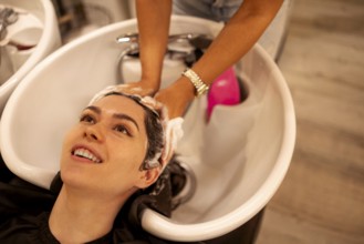 Cheerful young brunette womn enjoying head massage and washing hair while getting her haircare