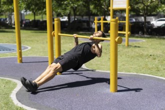 Young man performing inverted rows on outdoor bars.