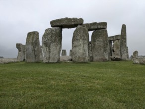 Close-up of Stonehenge with green grass and cloudy sky, emphasizing its ancient and historical