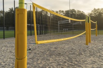 Yellow volleyball net stretching across a sandy beach volleyball court on a sunny day