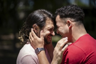 Couple of latin men hugging each other putting their heads together laughing in a park