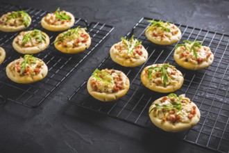 Small tarte flambee or mini pizza with onion, bacon and arugula on black background