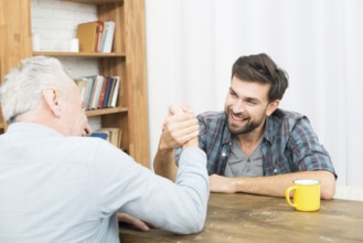 Aged man young happy guy with hands clasped arm wrestling challenge table room