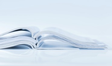 Stack of open magazines in blue tone on white background with copy space