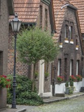 A quiet alley with brick houses, a alleyway lamp and a tree, flowers hanging from the windows,