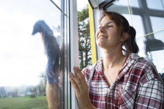 Woman manually washes the window of the house with a rag with spray cleaner and mop inside the