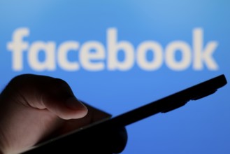 In this photo illustration, the Facebook logo seen in the background of a silhouette people holding