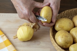 Hands peel potato, peelings on wooden cutting board