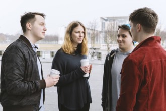 group of teenage friends having a conversation while standing together on city street holding