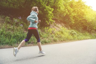 A young blonde woman running is practicing outdoors in a city mountain park in the forest. Warm