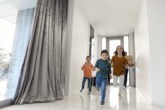 Happy family running in hall. Funny kids jumping with carton box, parents laughing, play with