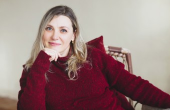 Attractive middle aged happy woman sitting and relaxing on comfortable chair at home on weekend,