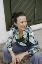 Smiling, dark-haired woman, 40+, sitting on a staircase