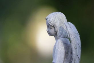 Sad looking little angel figure on a gravestone in front of atmospheric bokeh in the background