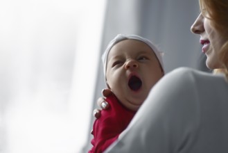 Mother holding cute newborn baby girl in her arms. Sleepy baby yawning