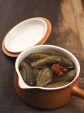 Organic gherkins in a rustic ceramic bowl on a wooden kitchen table, healthy food