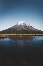 A snow-capped mountain reflected in a still lake under a clear blue sky, Mount Taranaki, New