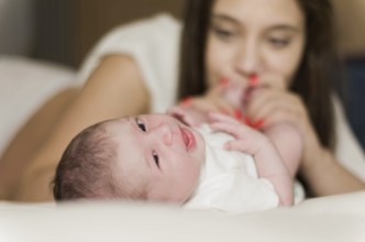 Young caring mother playing with her newborn son on the bed, happy moments of motherhood
