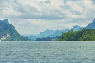Distant mountains on a cloudy horizon overlook a vast lake, offering a calm natural scene, Cheow